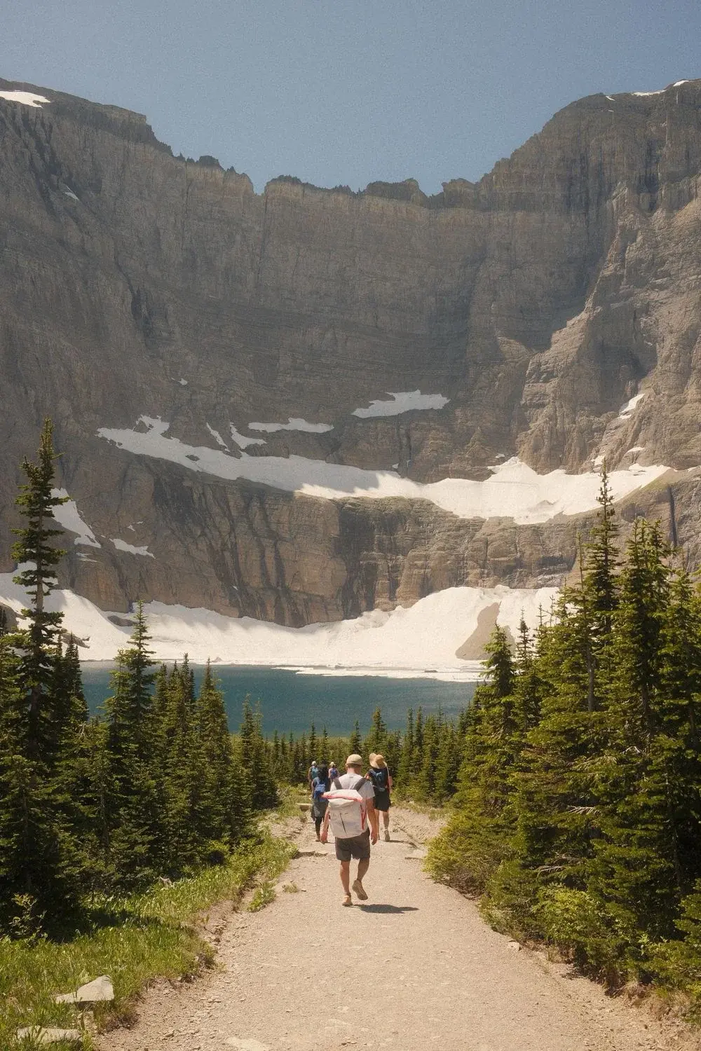 Hikers on a trail toward an alpine lake in Glacier National Park